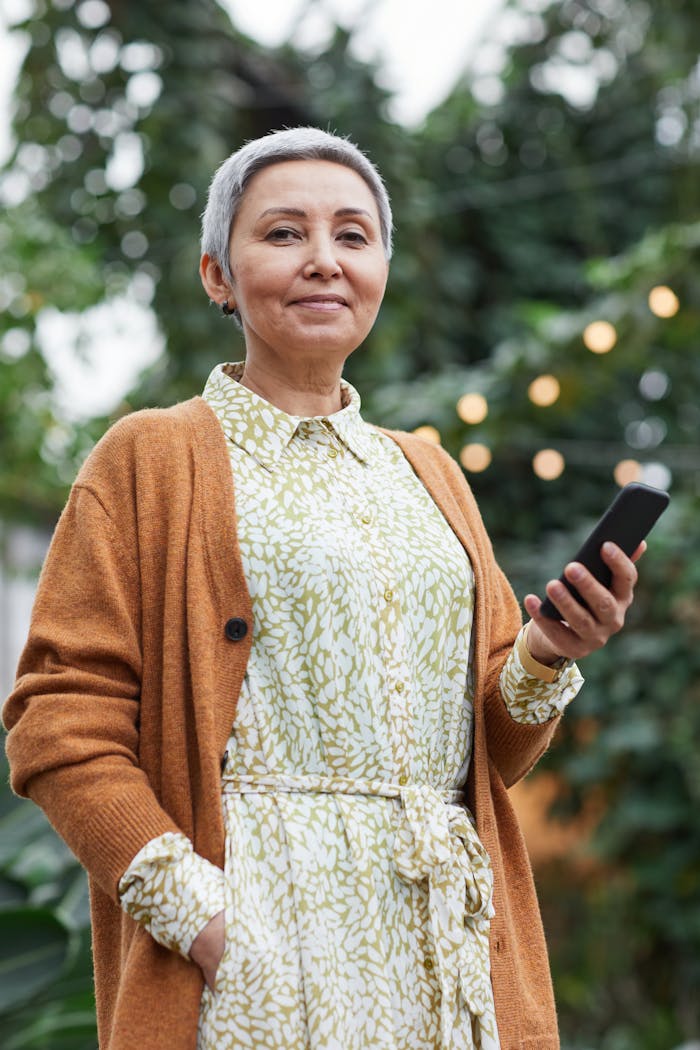 Cheerful senior woman in a garden holding a smartphone, embracing technology and connectivity.